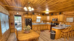 L’intérieur d’un chalet en bois comprend une table à manger, des chaises, une cuisine équipée d’un four à micro-ondes et une poubelle.