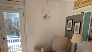 Ein Wohnzimmer mit einem floralen Teppich, beigen Sesseln, einem Beistelltisch mit Lampe und einer Wandleuchte.