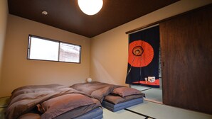 Huone, jossa on tatami-matto lattialla, futon-patja, punaisella kuvioilla koristeltu liukuovi ja ikkuna, josta on näkymä.