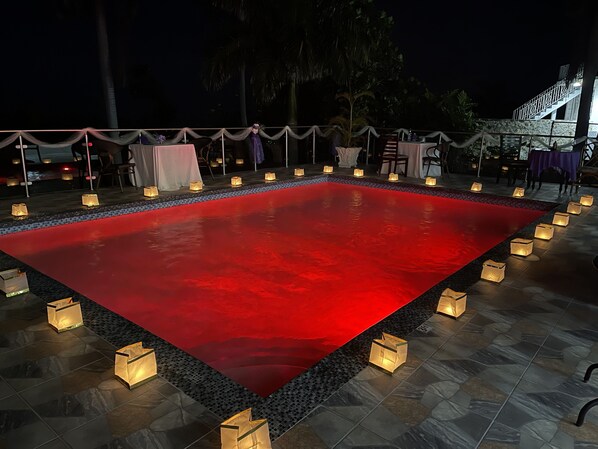 A rectangular pool with a red surface, surrounded by a tiled deck and small lanterns.