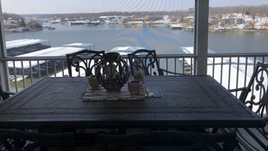 Un espace extérieur aménagé, abrité et doté de tables et de chaises, offrant une vue sur une étendue d’eau où l’on peut apercevoir des bateaux et des quais.