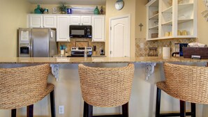 A kitchen with white cabinets, a microwave, a refrigerator, and a bar area with wicker chairs.