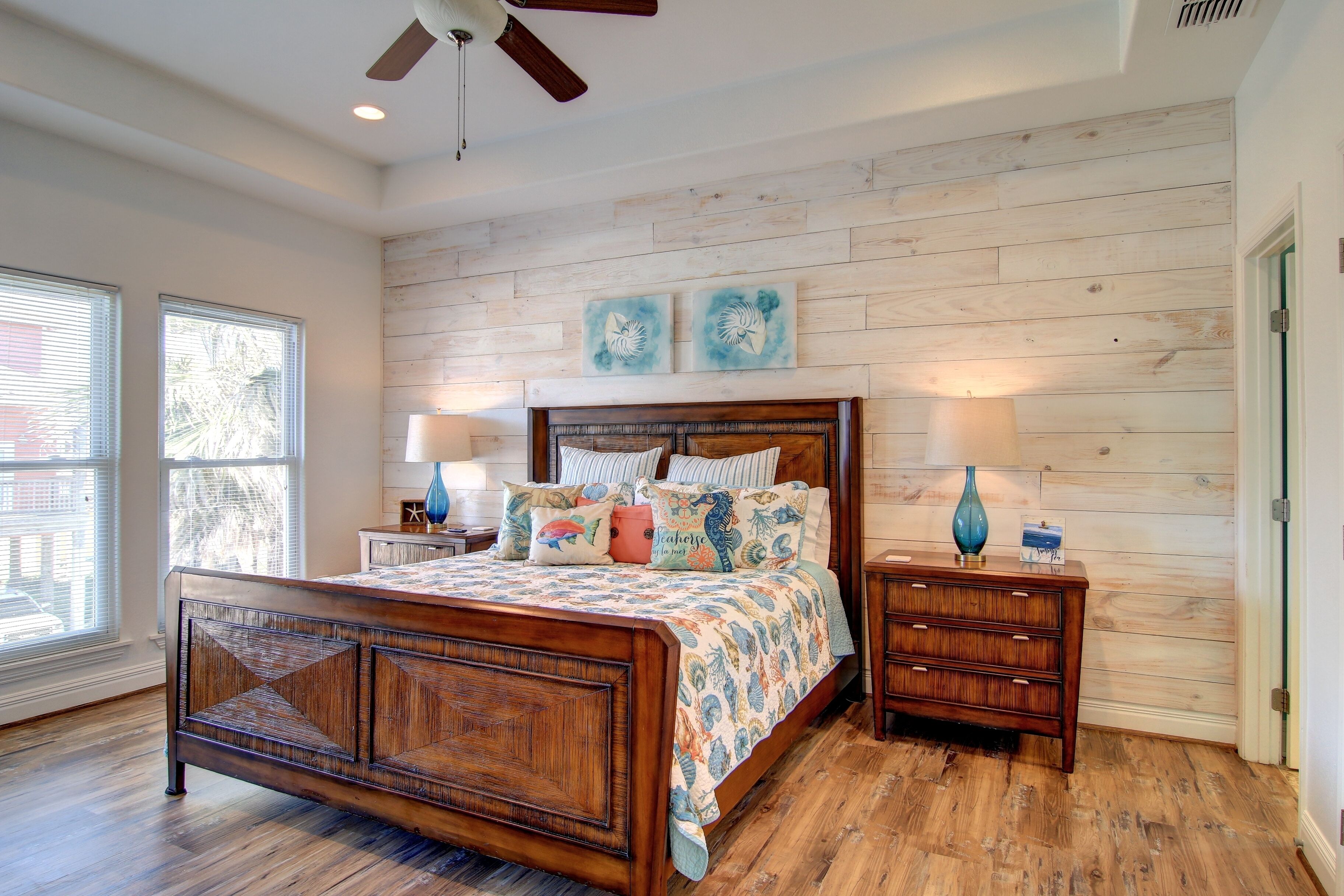 A bedroom with a wooden bed, two bedside tables, a ceiling fan, and a wall with wooden paneling.