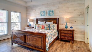 A bedroom with a wooden bed, two bedside tables with lamps, a wooden headboard, and a wooden wall panel.