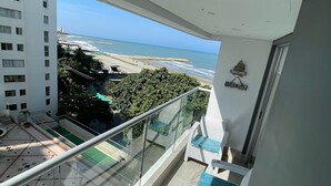 Un balcón con barandilla de vidrio que da a una playa y un edificio de gran altura.
