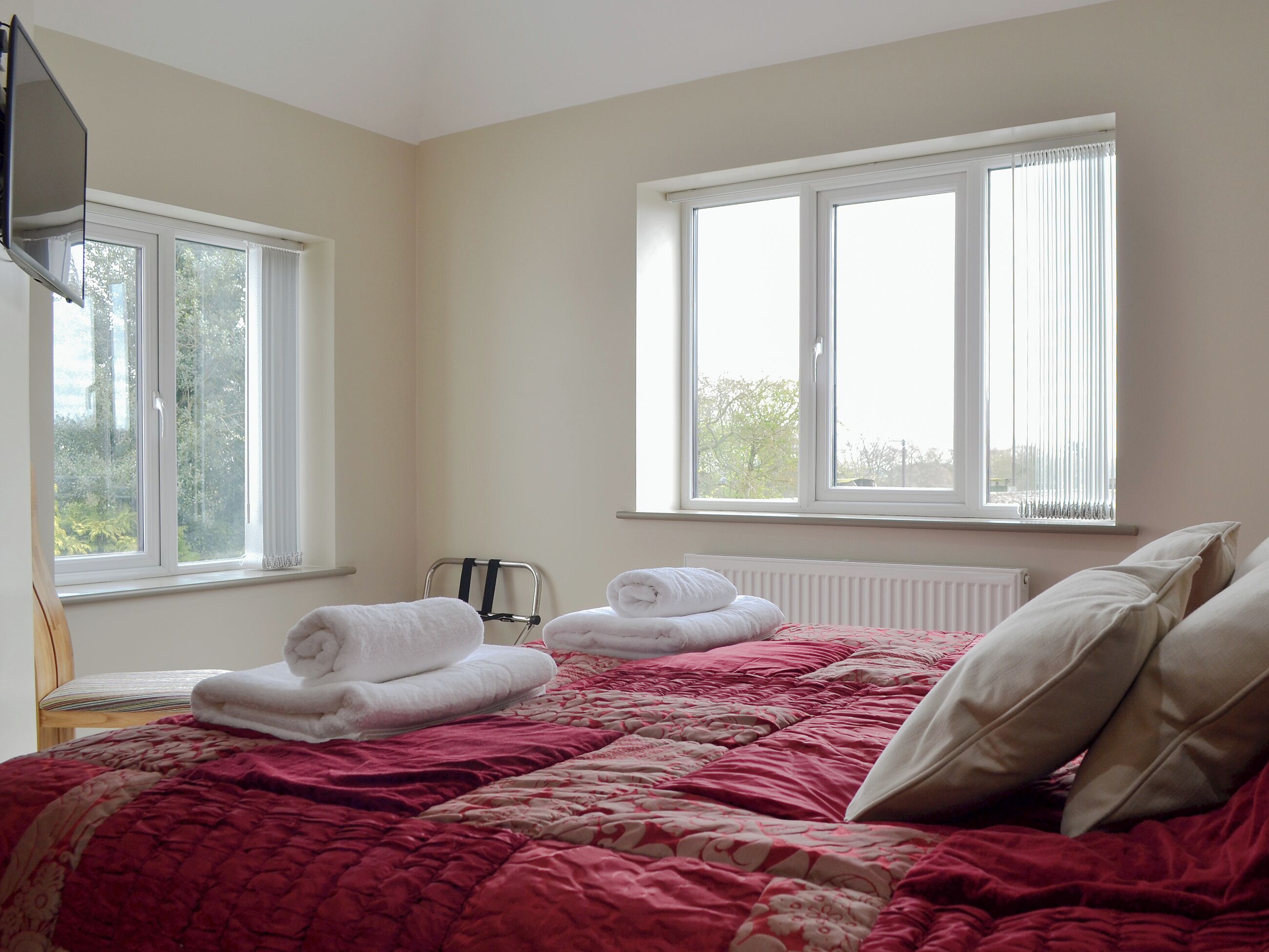 Quarto de hotel com uma cama, duas janelas, um radiador e uma cadeira.