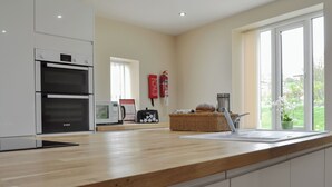 A modern kitchen with white cabinets, a Bosch oven, a microwave, and a toaster. There is a wooden countertop, a sink, and a window with a view of greenery outside. - 2 bedroom accommodation in Tibthorpe, near Driffield (Tibthorpe, near Driffield)