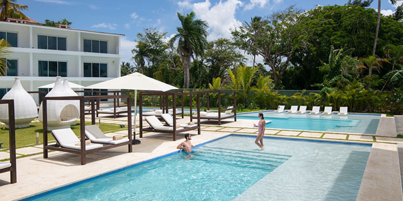 A swimming pool with lounge chairs and umbrellas, surrounded by lush greenery and a modern building.
