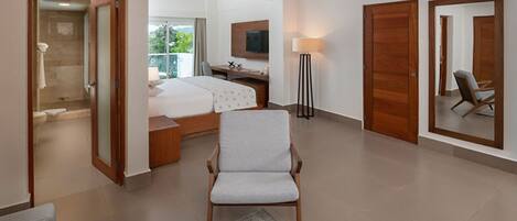 A hotel room with a bed, a desk, a chair, a TV, and a bathroom with a shower and toilet.
