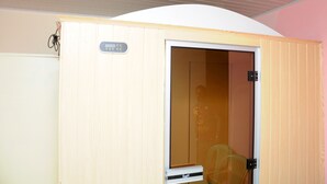 A sauna room with a wooden door, a control panel, and a chair inside. - Cityana Guest House (Addis Ababa)