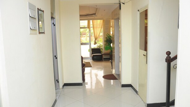A hallway with a tiled floor, a door on the right, and a view into a room with a chair and a plant. - Cityana Guest House (Addis Ababa)