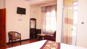 A hotel room with a large bed, a wooden chair, a small table, a television mounted on the wall, and a window with curtains. - Cityana Guest House (Addis Ababa)