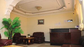 A reception area with a reception desk, two leather armchairs, a small table with a plant, and a large artificial palm tree. - Cityana Guest House (Addis Ababa)