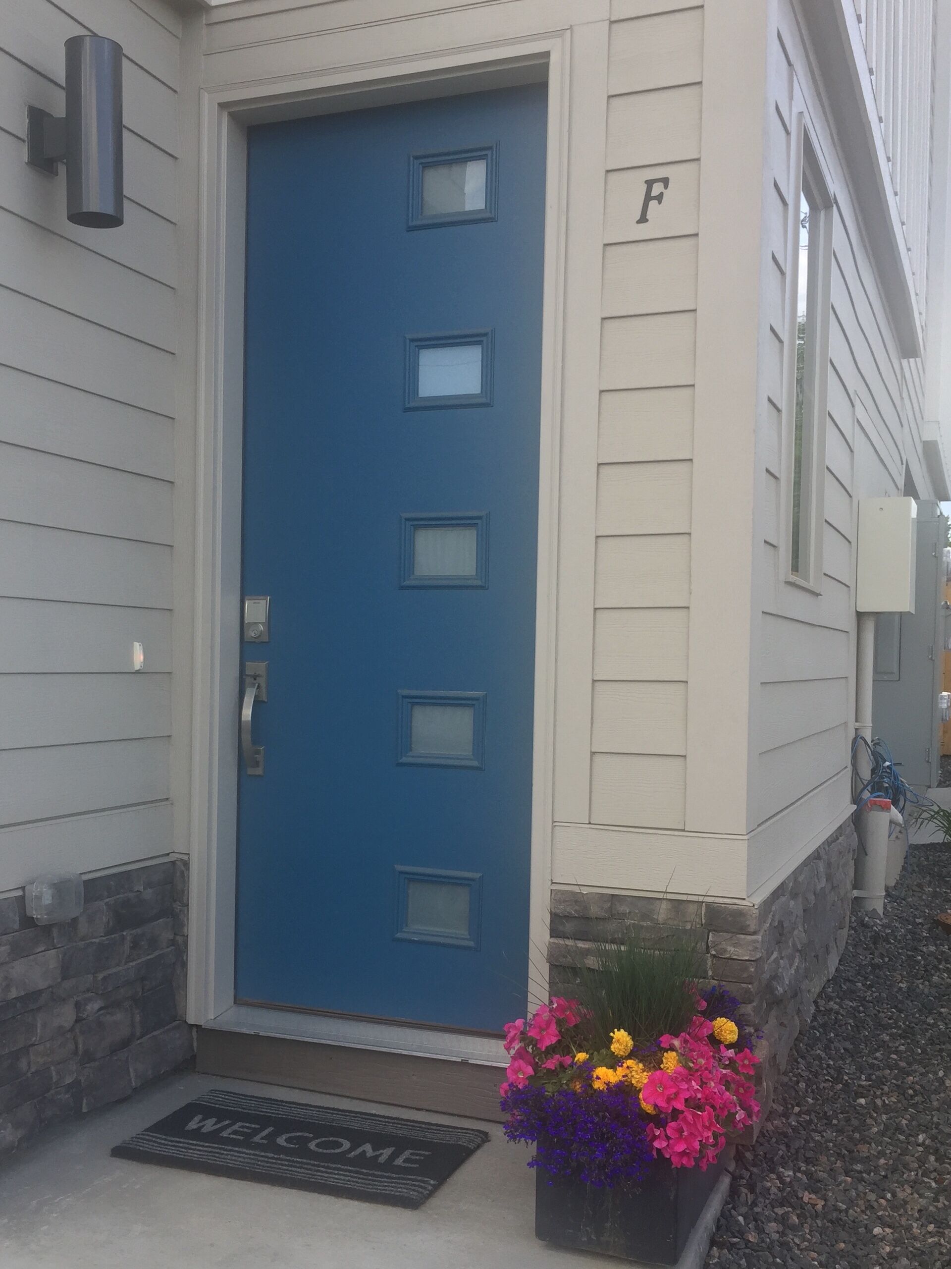 Une maison avec une porte bleue, un paillasson et un jardinière.