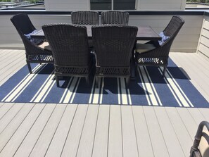 Una terraza con mesa y sillas, un tapete a rayas y un suelo de madera claro.
