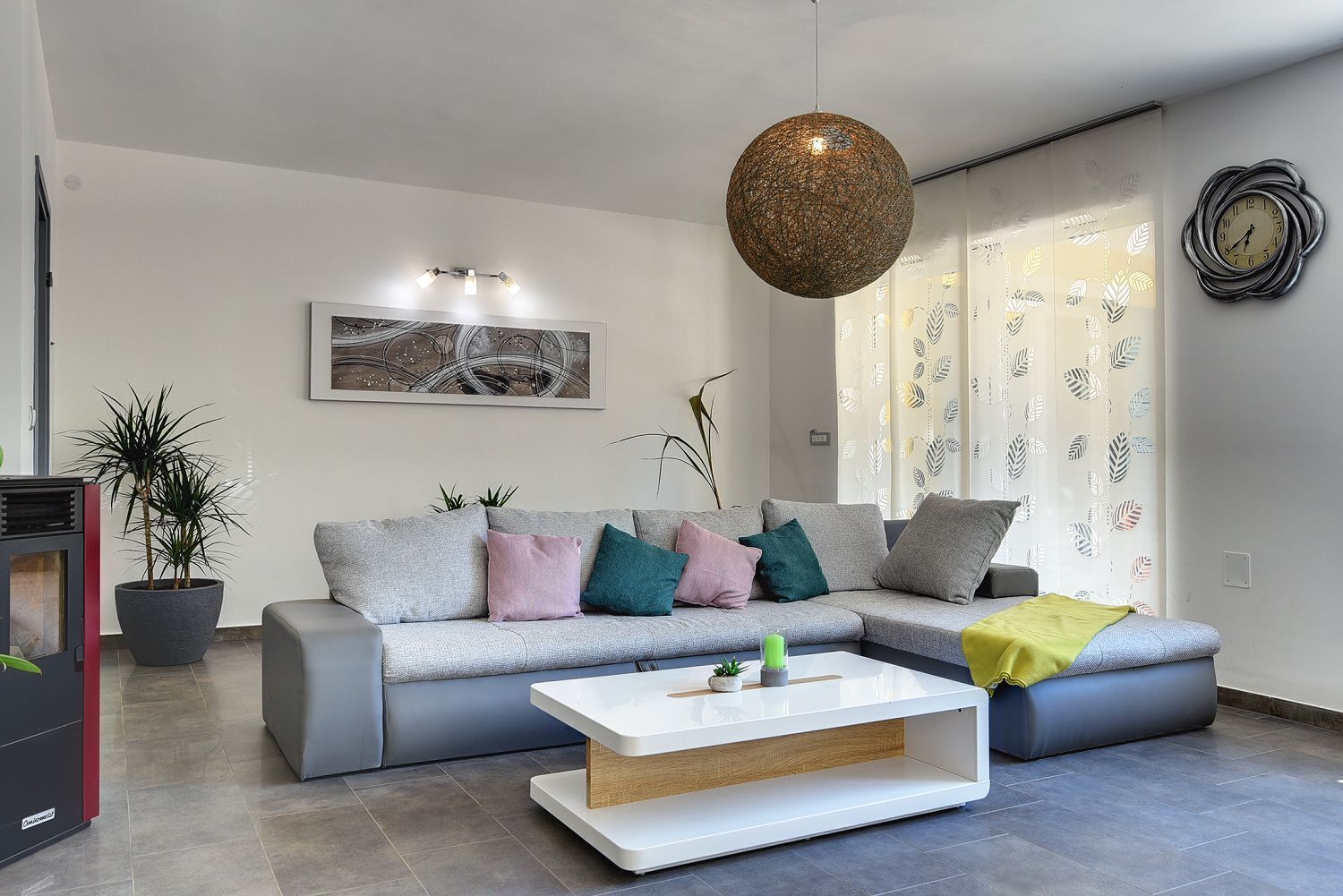 Una sala de estar moderna con un sofá gris, cojines coloridos, una mesa de centro blanca y una lámpara colgante.