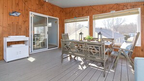 A covered wooden deck with a table and chairs, a white cabinet, and large windows. - Narragansett Pier! Easy walk to seawall, food, shopping, playground - more!  (Narragansett)