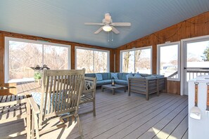 Une terrasse extérieure couverte, aménagée avec du mobilier en bois, notamment un canapé et des fauteuils, et dotée d’un ventilateur de plafond.