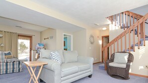 A living room with a sofa, a small wooden table, a wicker chair, and a staircase. - Narragansett Pier! Easy walk to seawall, food, shopping, playground - more!  (Narragansett)