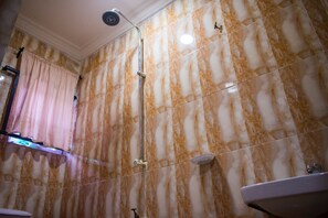 A bathroom with marble walls, a shower, and a sink. - White Rose Suites (Lagos)