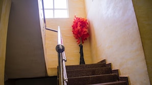 A staircase with marble steps and a metal handrail, leading to a landing with a window and a red flower arrangement. - White Rose Suites (Lagos)