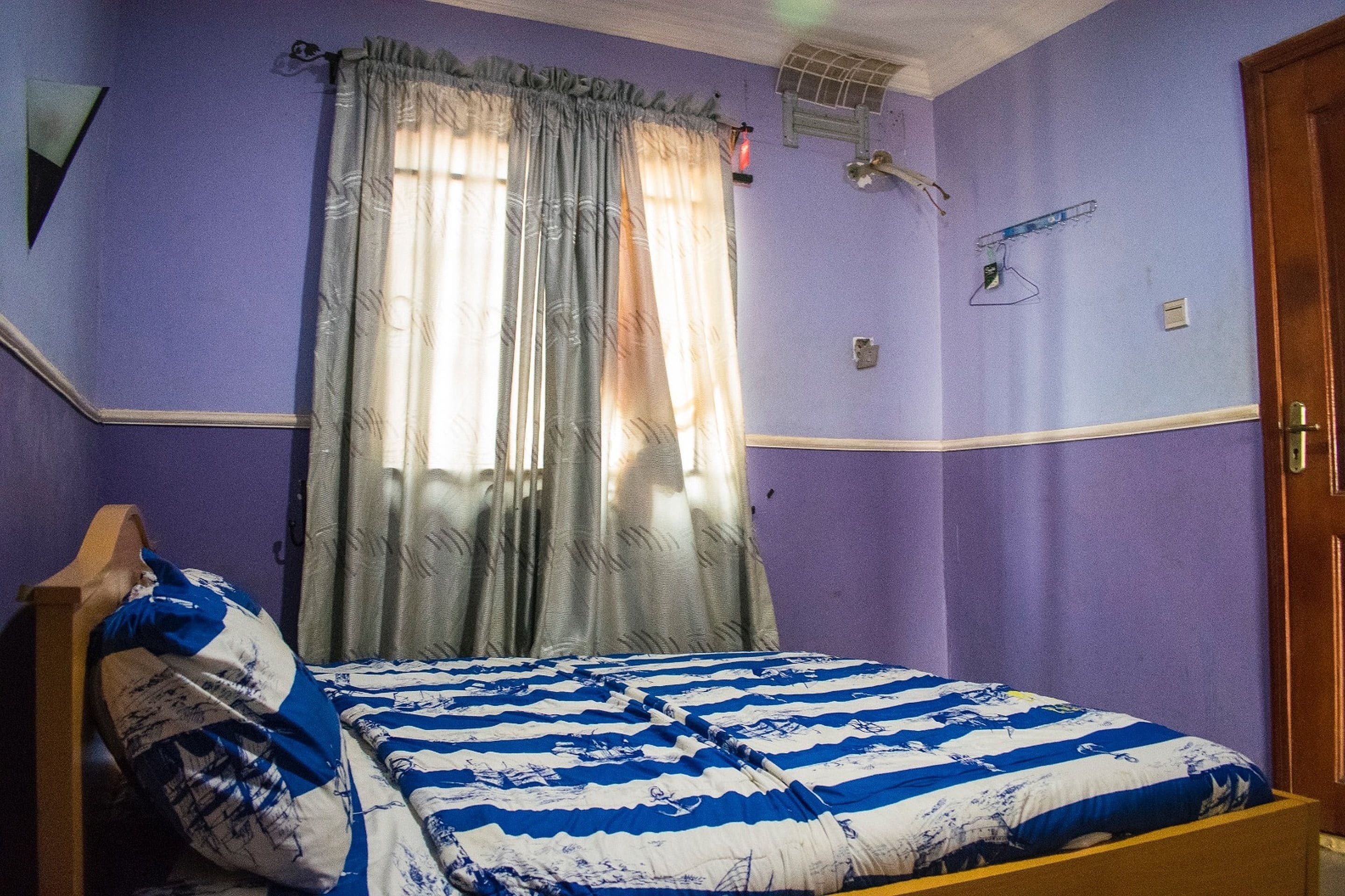A bedroom with a bed, a window with curtains, and a door.