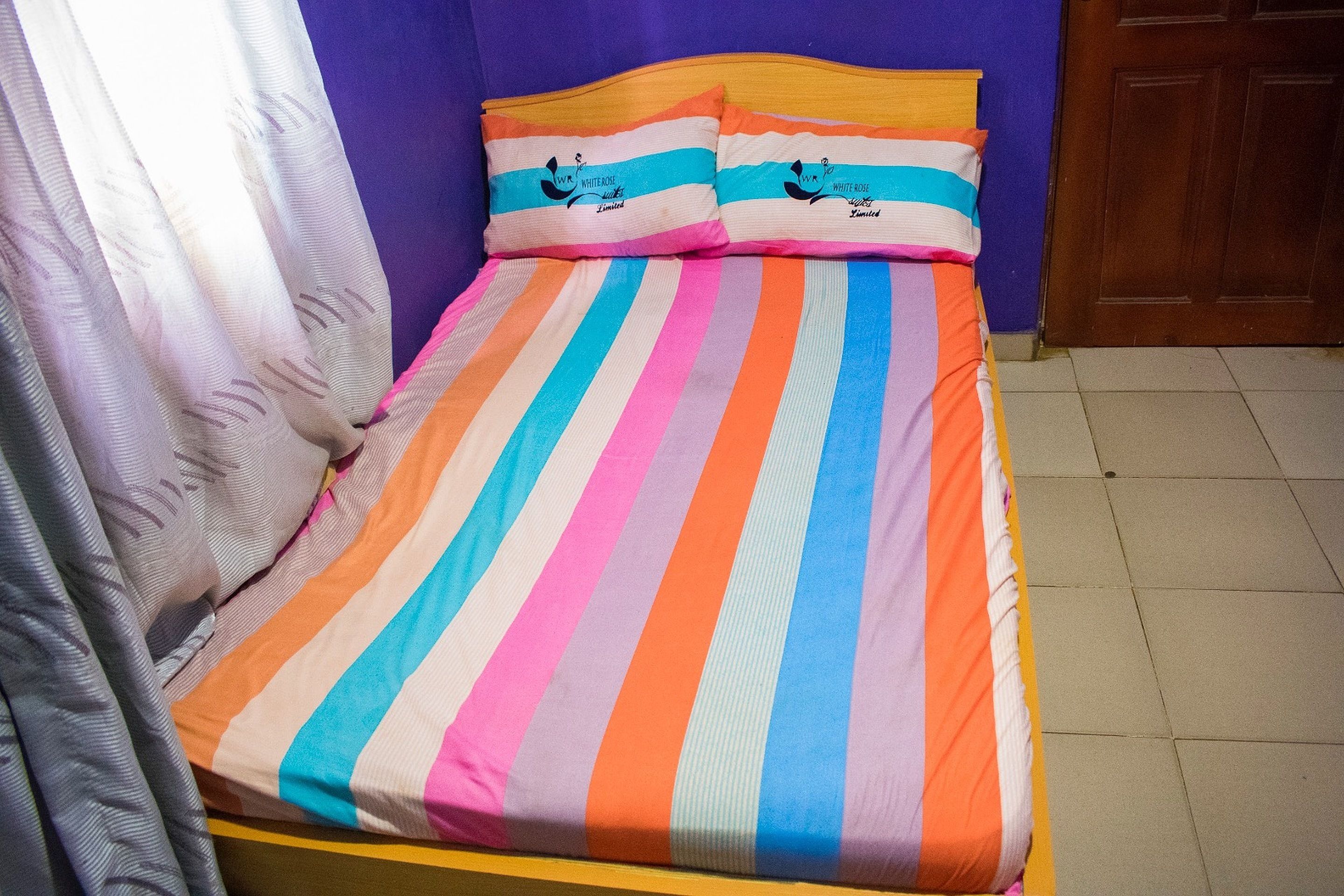 A bed with a striped bedspread and pillows, a wooden headboard, and a closed door in the background.