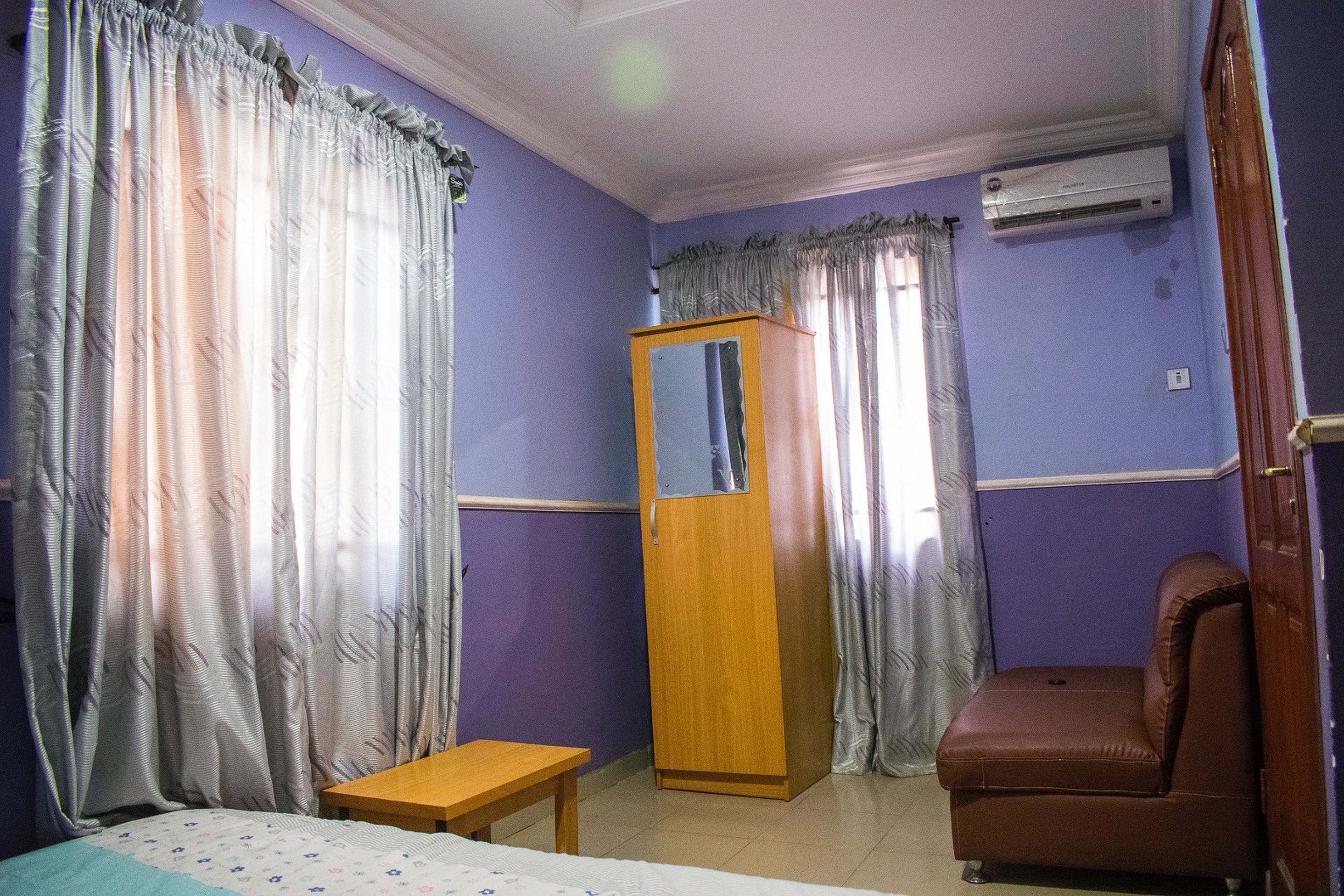 Una habitación con paredes moradas, un armario de madera, un sillón de cuero marrón y una mesita de madera.