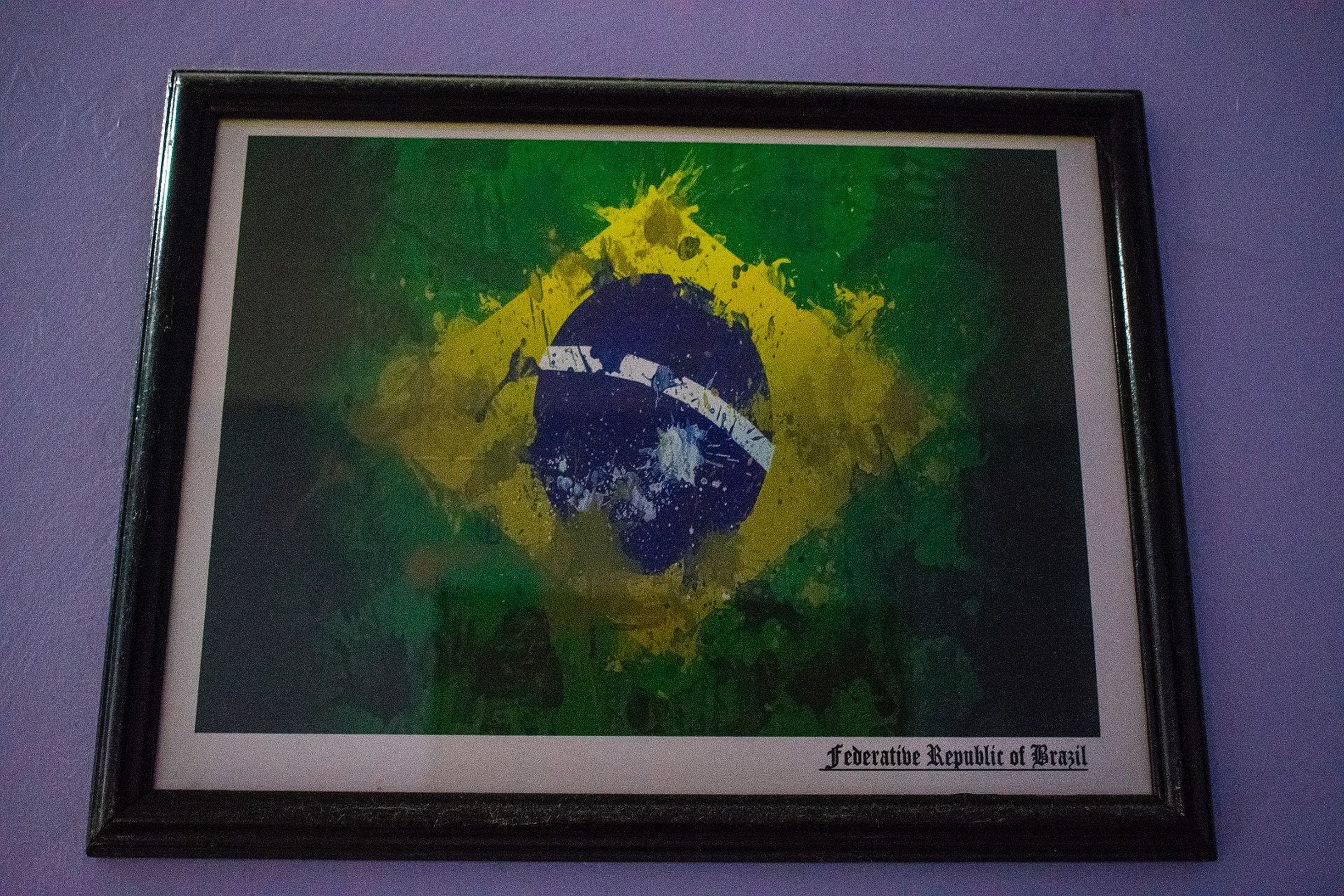 A framed picture of the Brazilian flag on a purple wall.