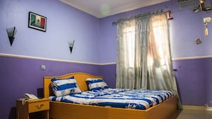 A bedroom with a wooden bed, a nightstand, a wall-mounted phone, and a flag on the wall. - White Rose Suites (Lagos)