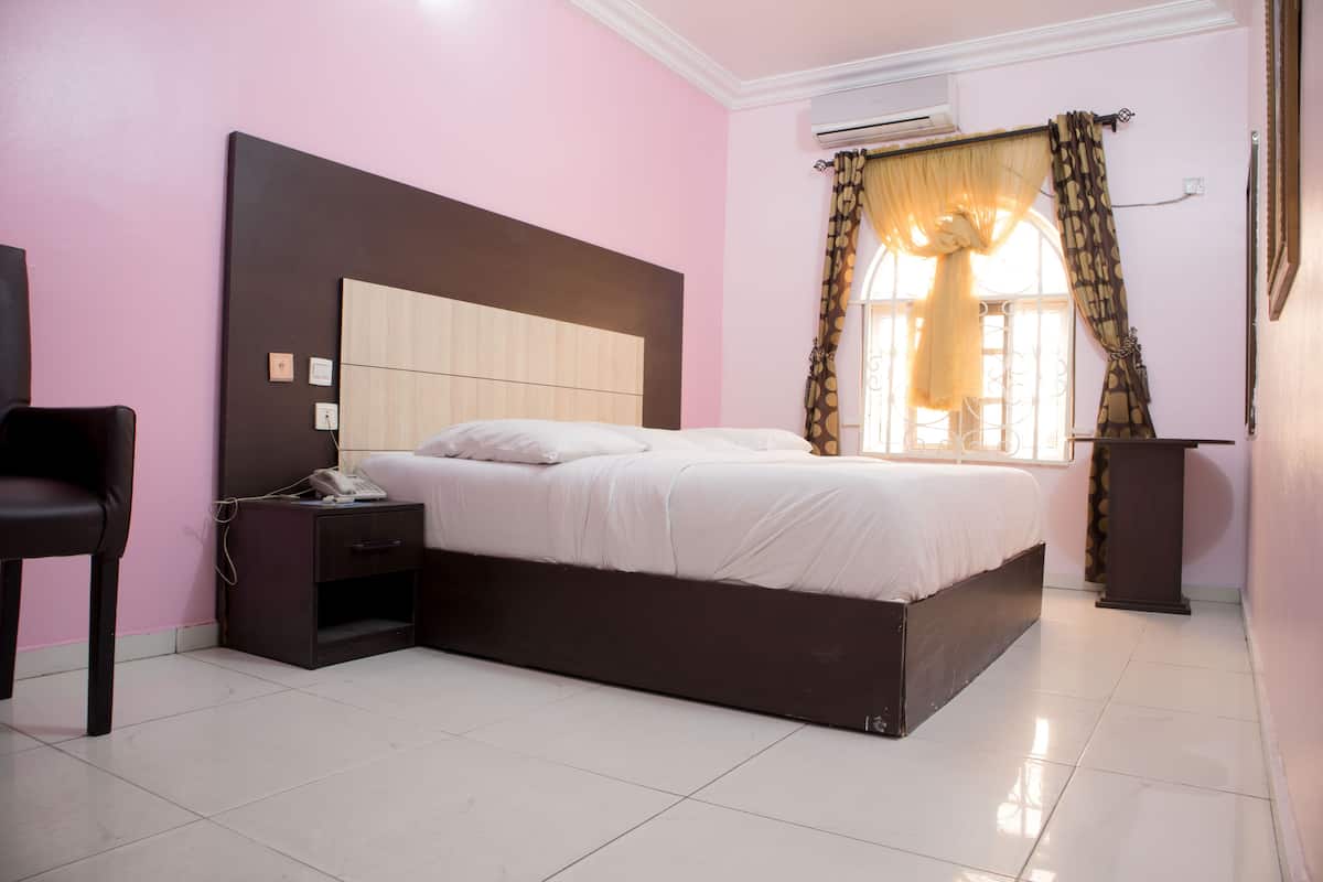 Une chambre à coucher avec un grand lit, une table de chevet, une chaise et une fenêtre avec des rideaux.