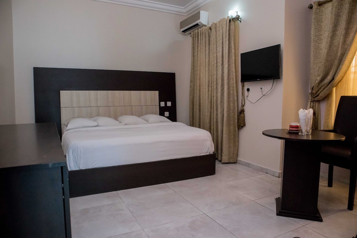 Une chambre d’hôtel avec un lit, un bureau, une chaise, une télévision et des rideaux.