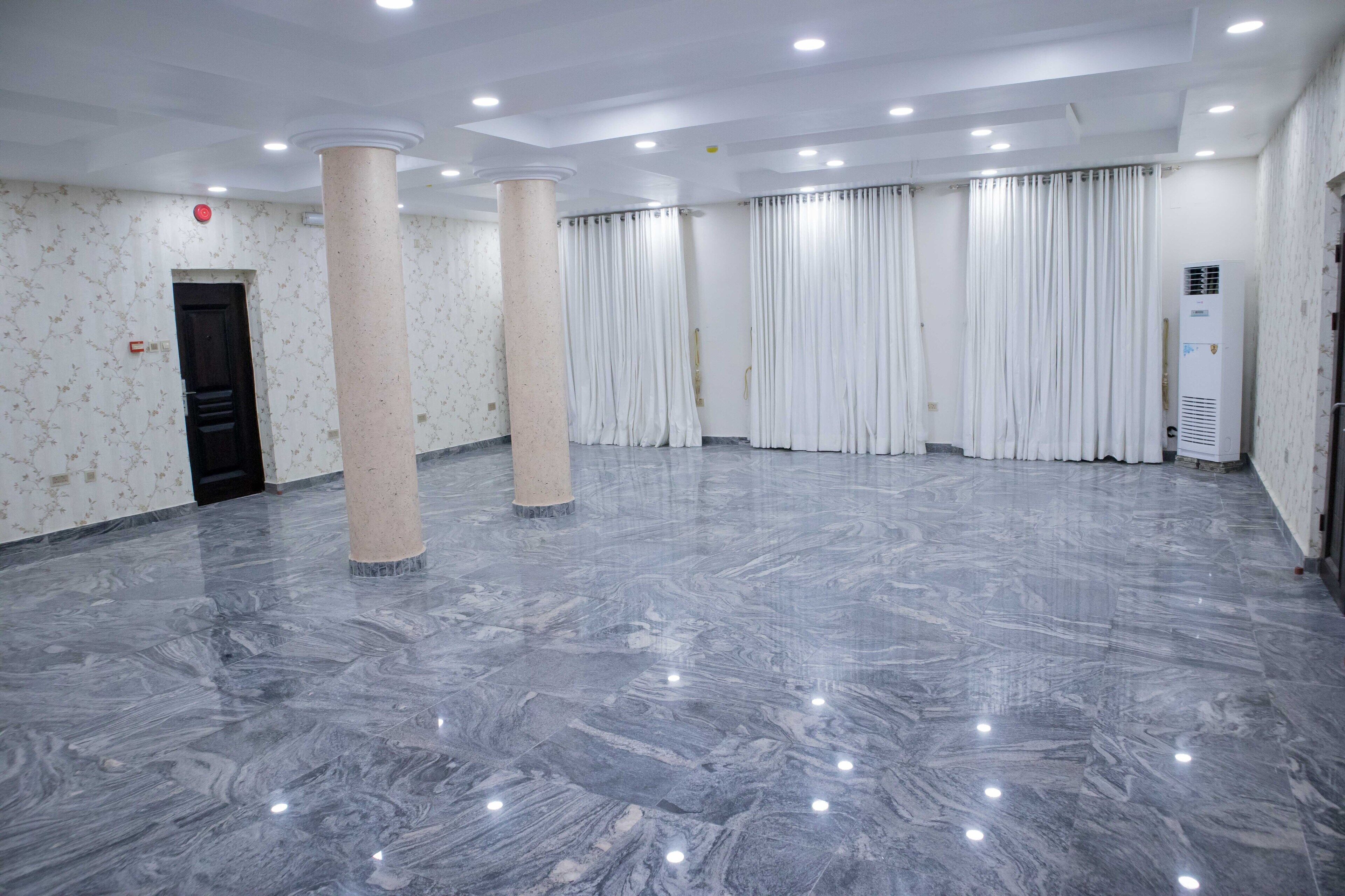 A spacious room with a marble floor, white curtains, and a column.