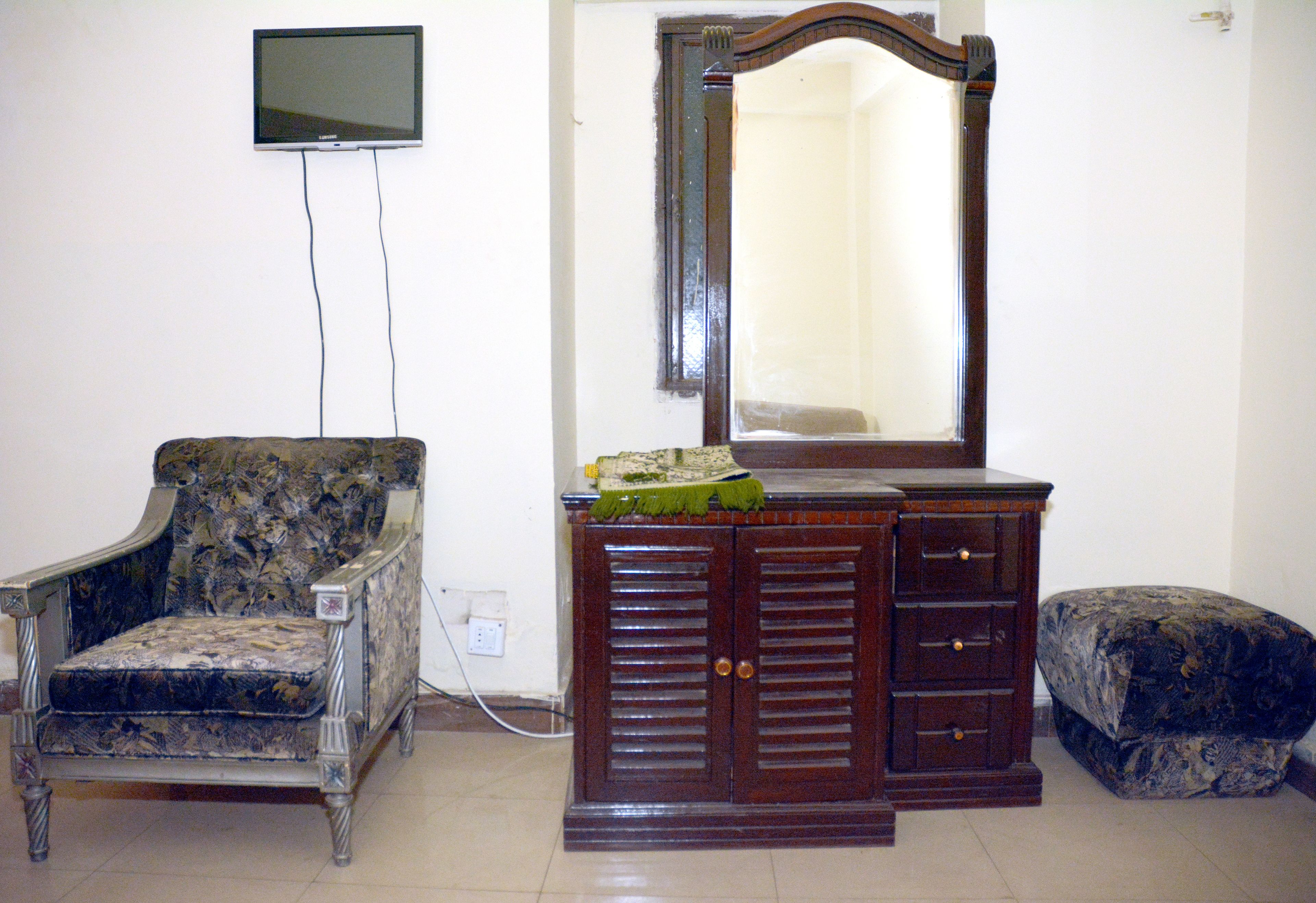A room with a wooden dresser, a chair, a mirror, and a television mounted on the wall.