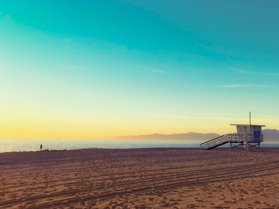 A beach with a lifeguard tower and a person standing on the sand.