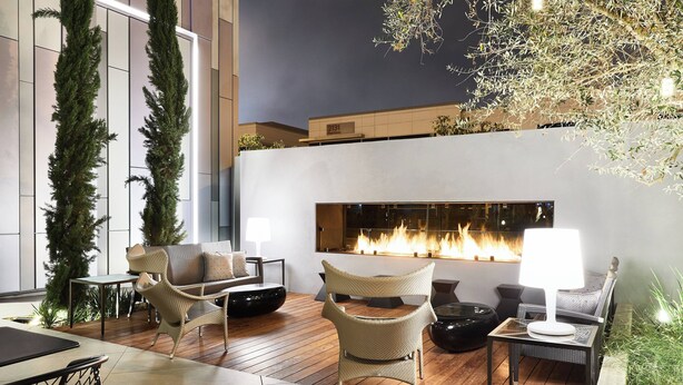 A modern outdoor lounge area with wicker furniture, a fireplace, and a view of the building's exterior.