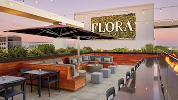 Relax in the FLORA's outdoor seating area, featuring a bench, table, and umbrella, surrounded by a low wall and a cozy fire feature.