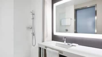 A modern bathroom with a glass shower enclosure, a white sink, and a large mirror above the sink.