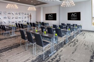 A conference room with multiple tables and chairs, AC Hotels Marriott branding, and a patterned carpet.