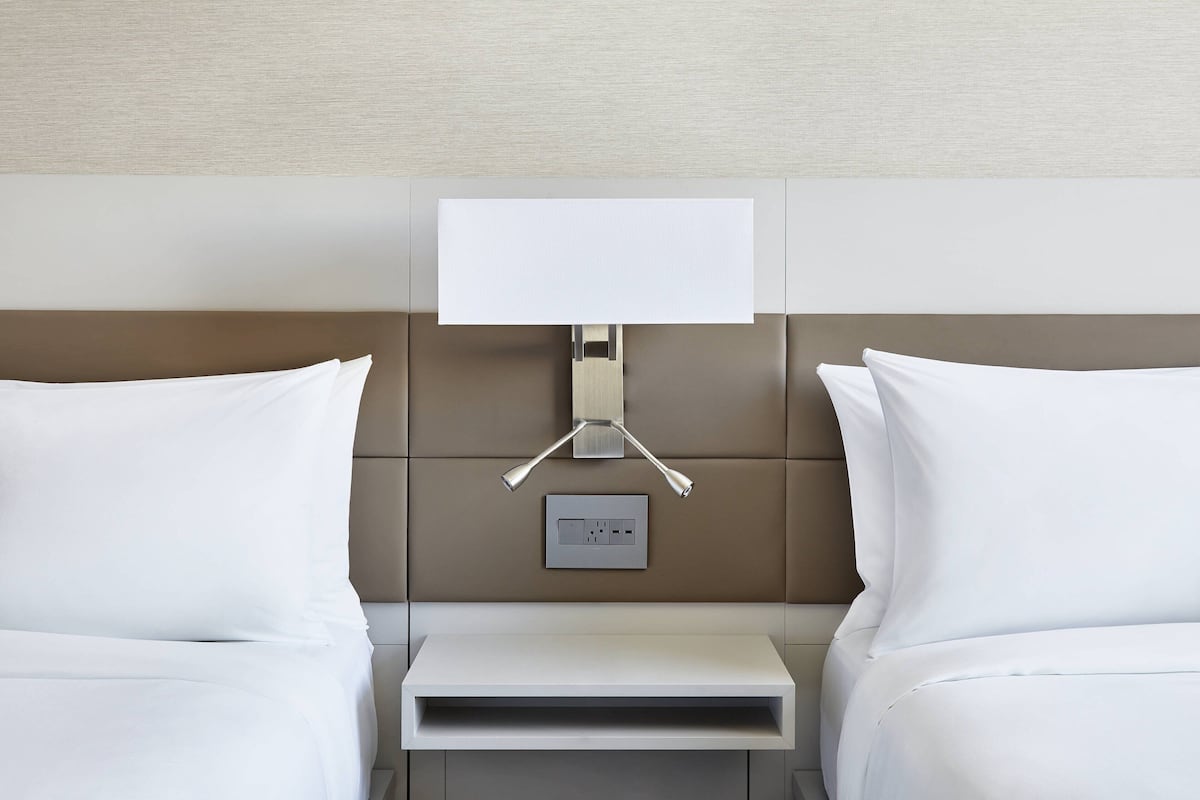 A hotel room with a bed, bedside table, lamp, and electrical outlet.
