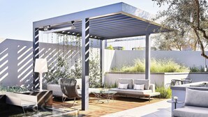 A modern outdoor patio with a pergola, seating area, and a small water feature.