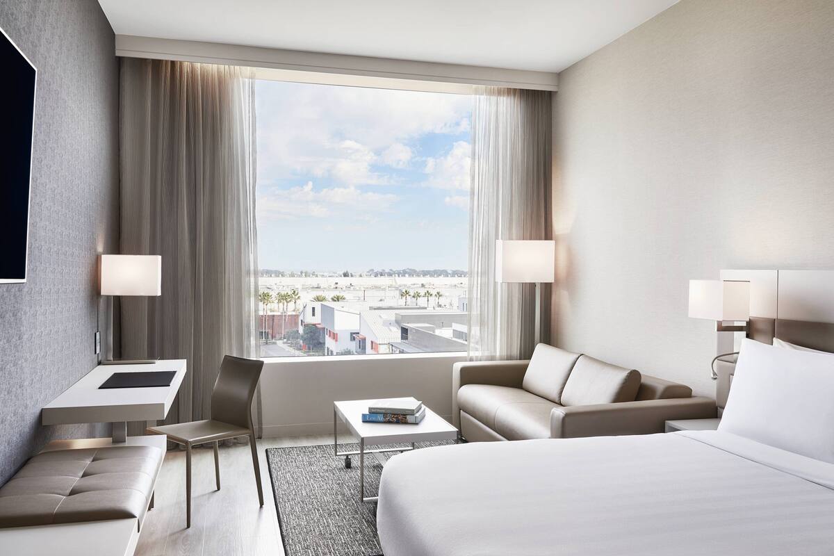 A hotel room with a bed, two sofas, a small table, a desk, and a TV.