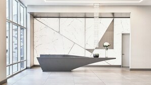 A modern reception area with a marble wall, a reception desk, and a large window offering a view of the city.