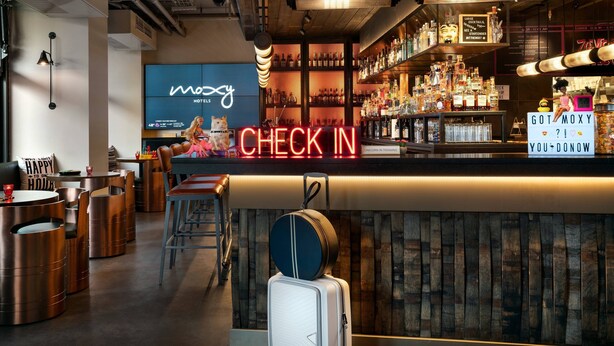 Zona de bar con un letrero de neón que dice 'CHECK IN', una variedad de botellas de licor y una disposición de asientos moderna.