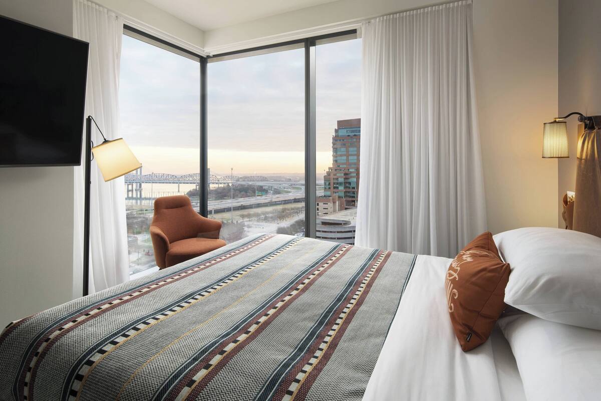 Une chambre d’hôtel avec un grand lit, une chaise, une télévision et une vue sur un pont et des immeubles.