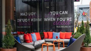 An outdoor seating area with a gray sofa and orange tables, surrounded by potted plants.