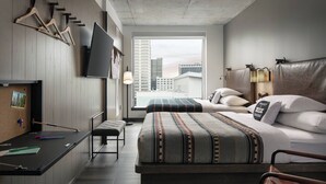 Una habitación de hotel moderna con una cama grande, un escritorio con silla, un televisor en la pared y un ventanal con vista a la ciudad.