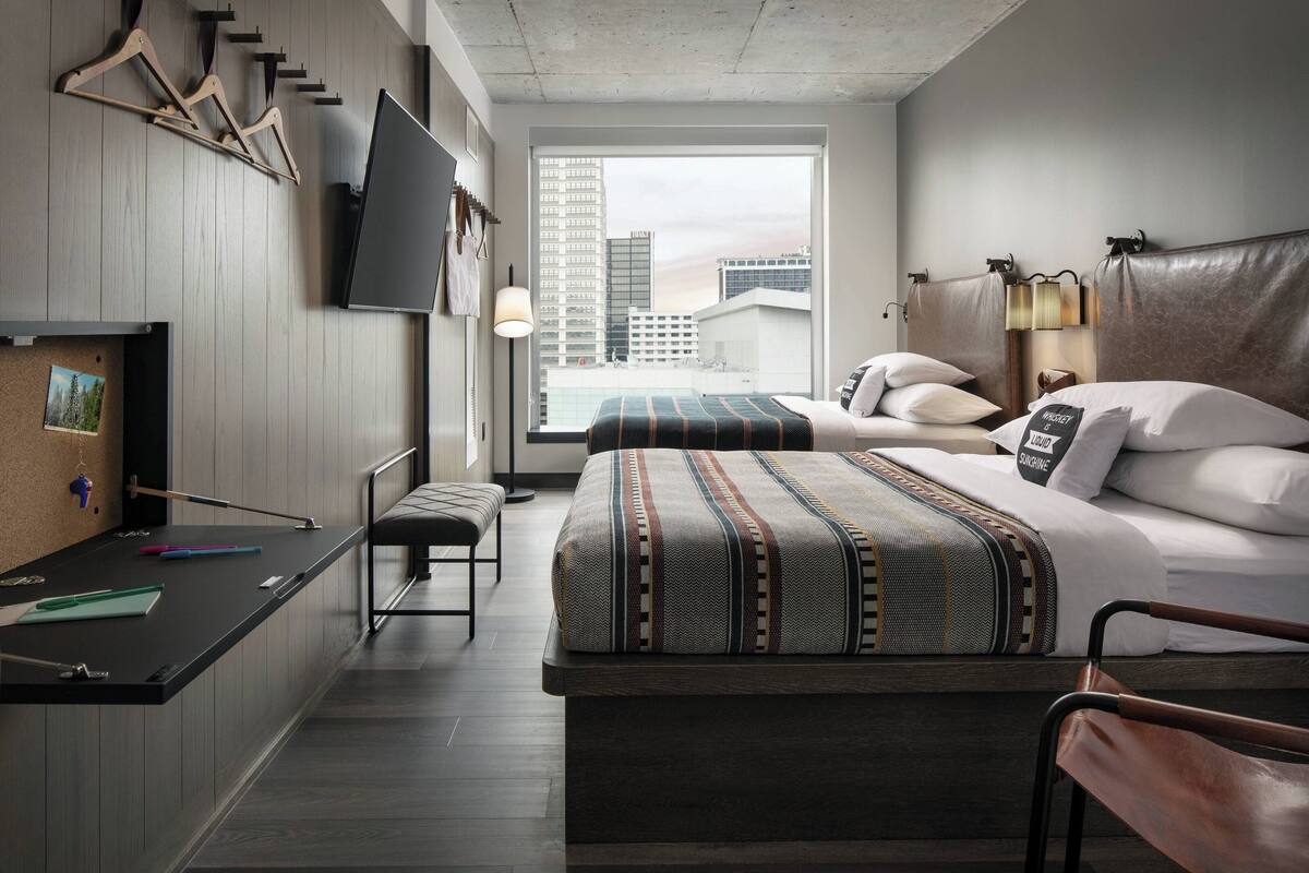 Une chambre d’hôtel moderne dotée d’un grand lit, d’un bureau avec une chaise, d’un téléviseur fixé au mur et d’une fenêtre donnant sur la ville.