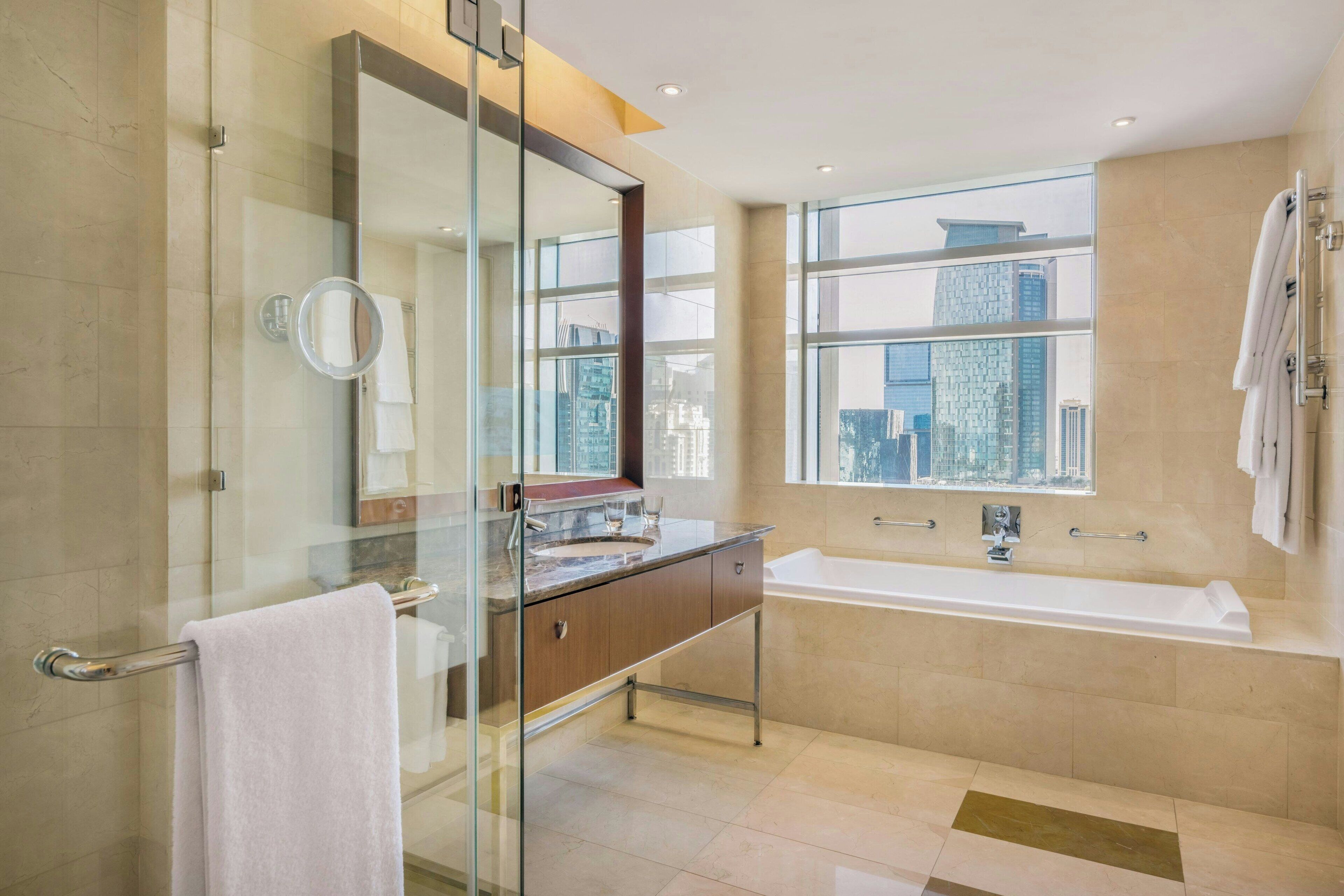 Un baño moderno con cabina de ducha de vidrio, un espejo grande, tocador con lavamanos y bañera.