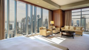 Amplia habitación de hotel con una cama grande, dos sofás, una mesa de centro y vistas del horizonte de la ciudad a través de ventanas de piso a techo.